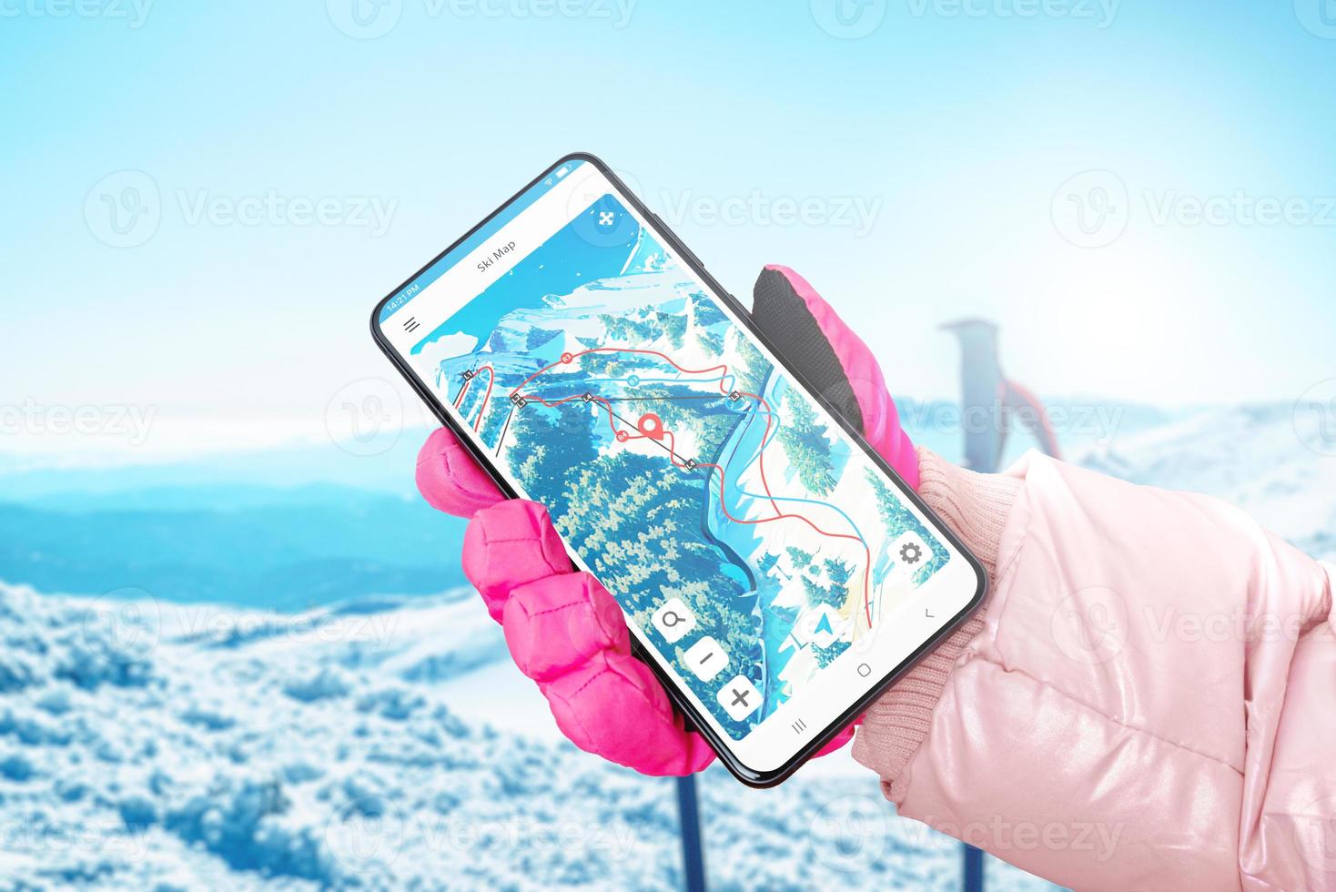 Ski map on phone display in hand with glove. Ski poles and mountain in background photo