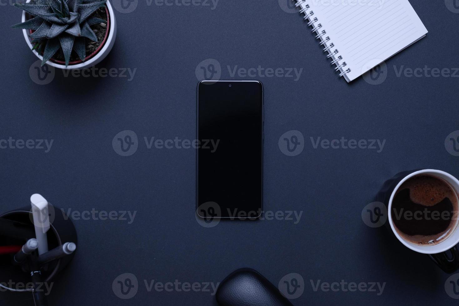 Blank mobile phone on black desk surrounded by office supplies. Business composition, top view, flat lay representing the integration of technology in contemporary work environments photo