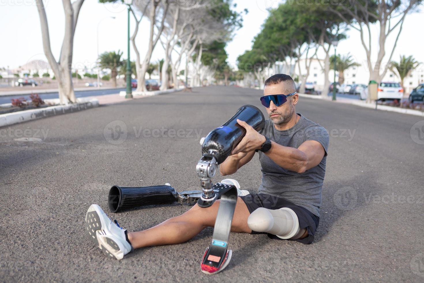 hombre amputado sentado en la carretera y poniéndose una pierna artificial foto