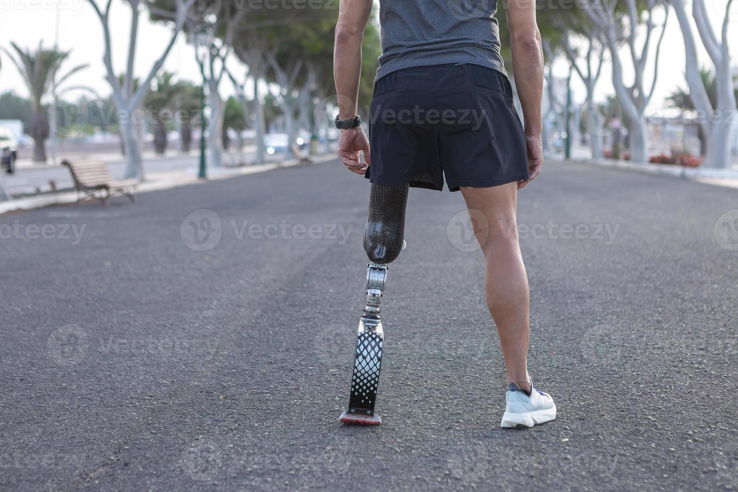 Crop runner with artificial blade leg standing on asphalt road photo