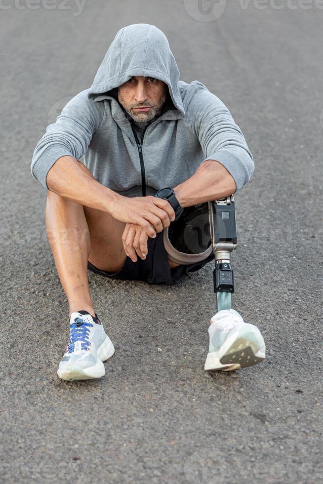 Handicapped male athlete sitting on asphalt road photo