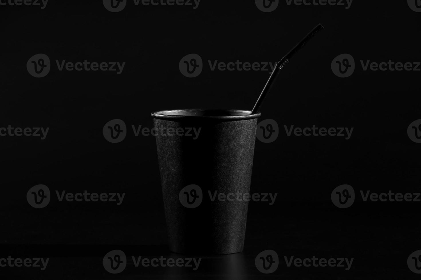 black paper glass with a tube on a black background. a glass of coffee or tea with a plastic cover photo