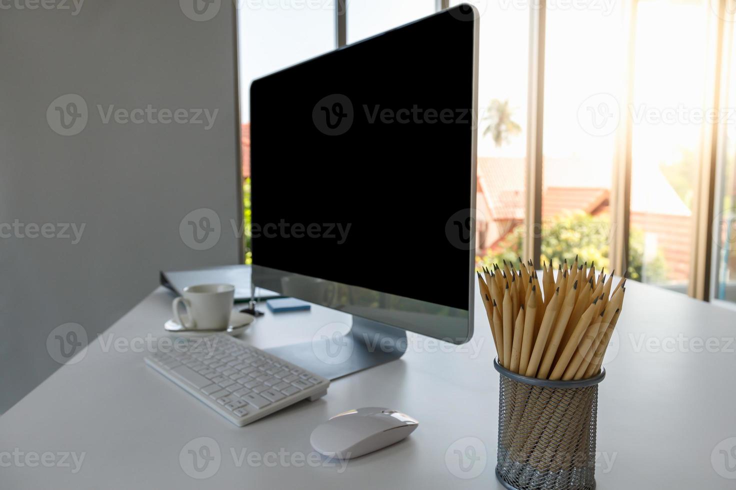 vista del escritorio de la computadora de la sala de oficina con espacio de copia de pantalla en blanco, teclado, mouse, taza blanca de café y lápiz. usando como concepto de negocio y trabajo. foto