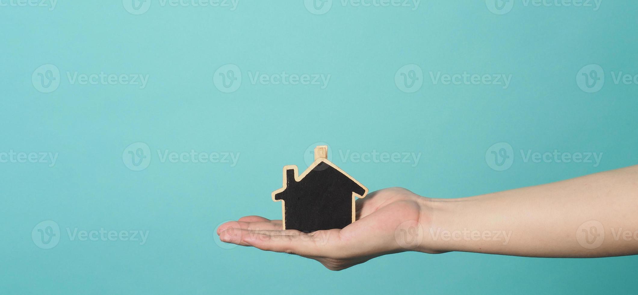 Small wood house in hands represent concepts such as home care family love real estate housing shelter insurance and mortgage. Hands holding small model house isolated on blue green studio background. photo