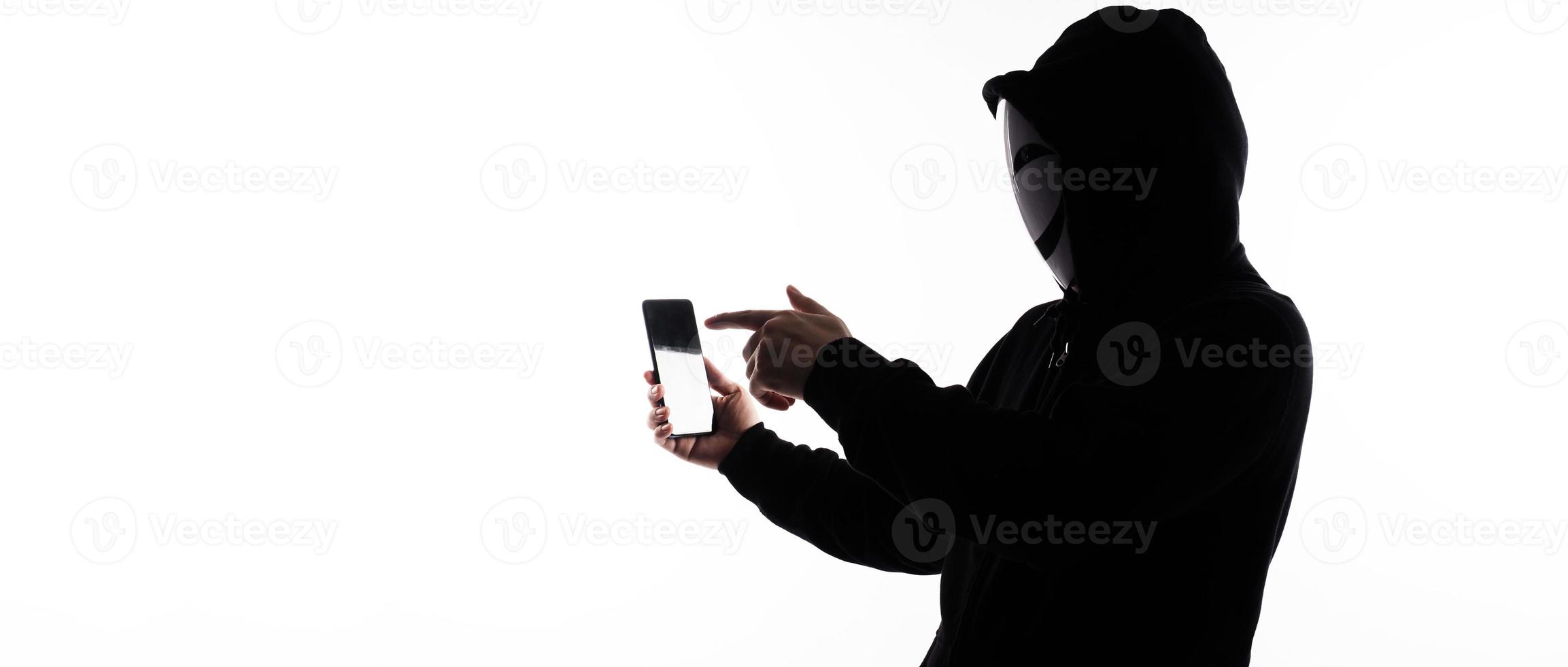 hacker anónimo y mascarilla con smartphone en la mano. hombre con camisa de capucha negra sosteniendo y usando un teléfono móvil con fondo blanco. representan el concepto de piratería informática o robo de datos personales foto