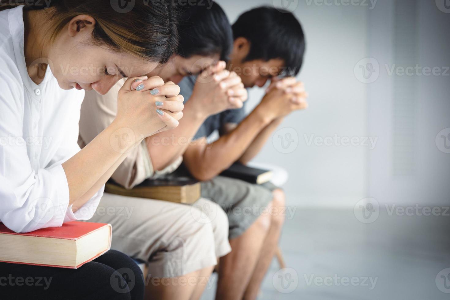 A group of Asian Christians sits inside a Catholic Church praying for God's blessing, the pale sun shining in the place of worship with copy space. photo