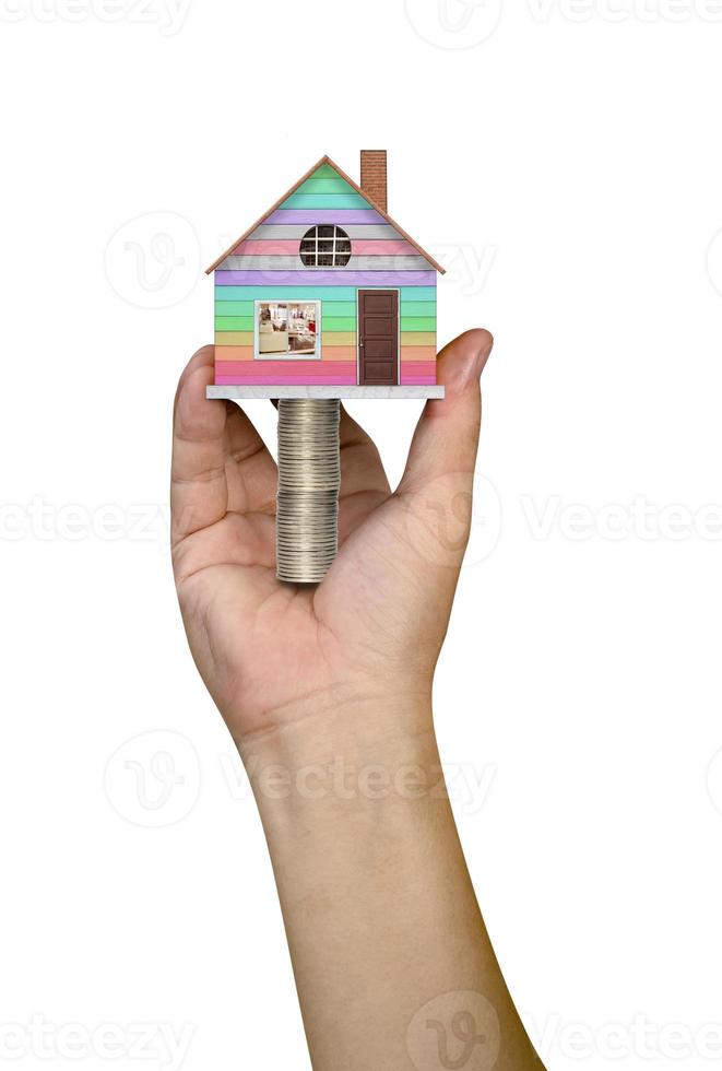 hand holding a house with piles of coins on white background photo