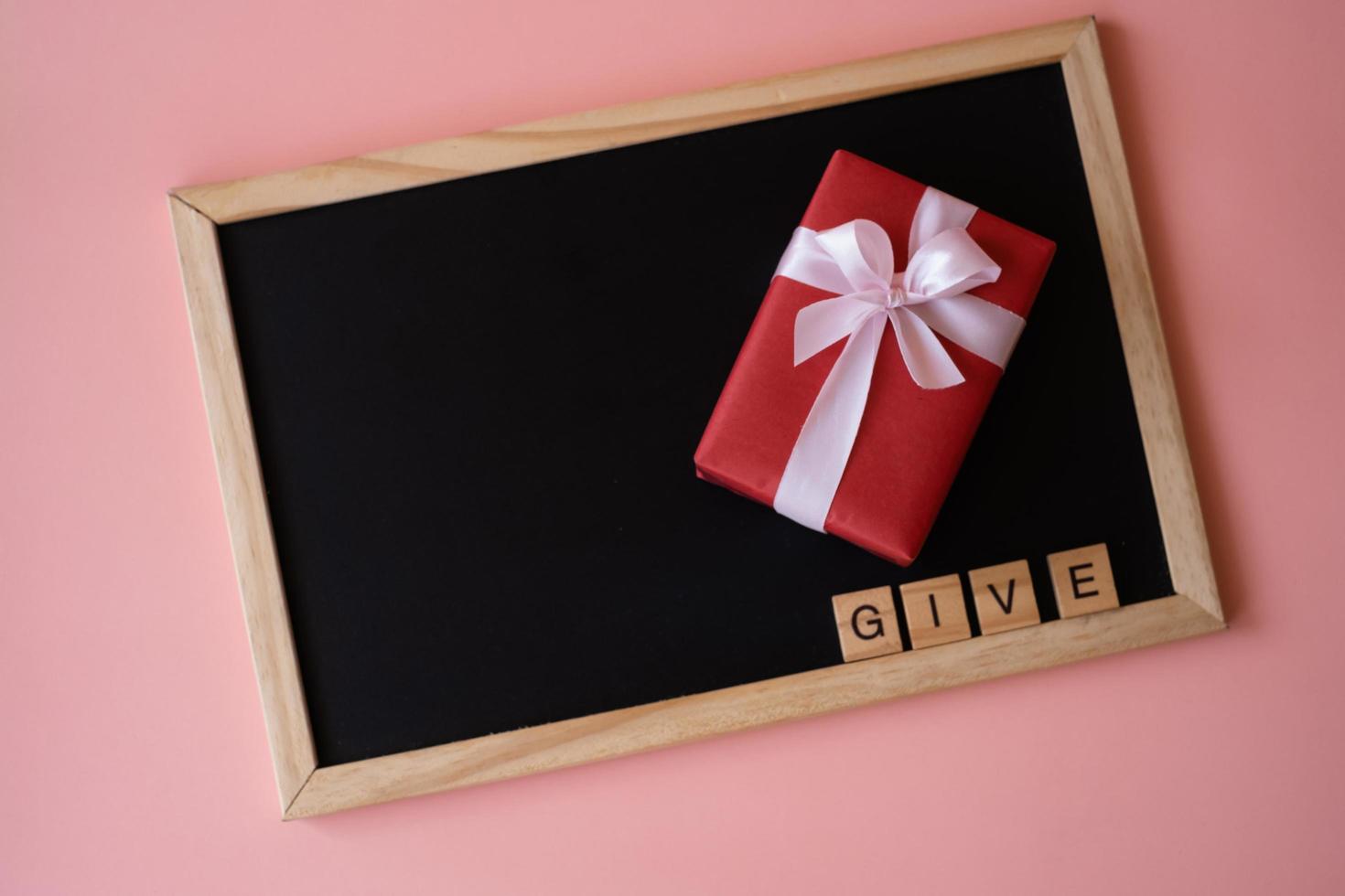 Red gift box and letter words of give on the black board on pink background. photo