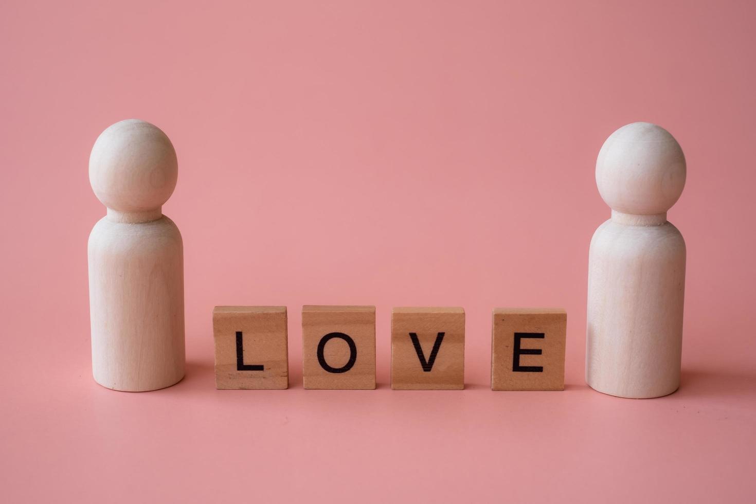 Letter words of love between wooden figurines of man and man on pink background. Love LGBTQ concept. Sexual minorities and communities concept photo