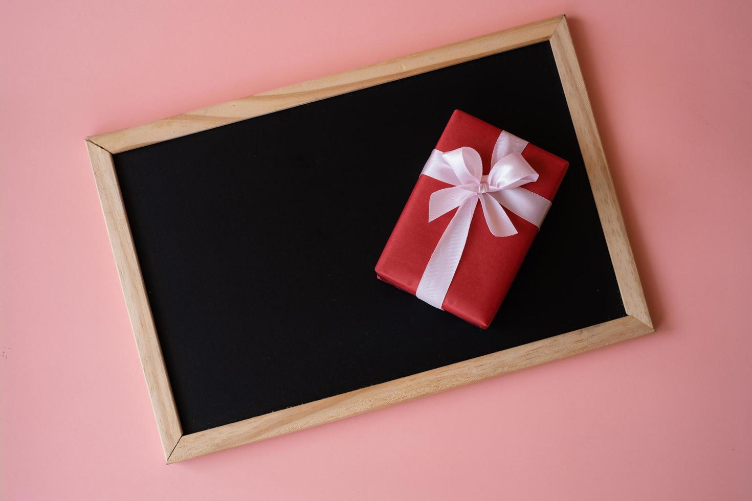 caja de regalo roja en la pizarra negra aislada en fondo rosa. foto