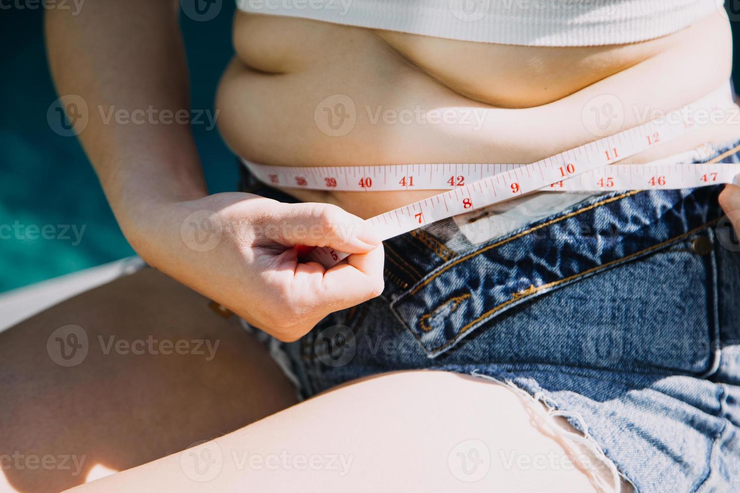 mujer gorda, barriga gorda, gordita, mujer obesa mano sosteniendo grasa abdominal excesiva con cinta métrica, concepto de estilo de vida de dieta de mujer foto