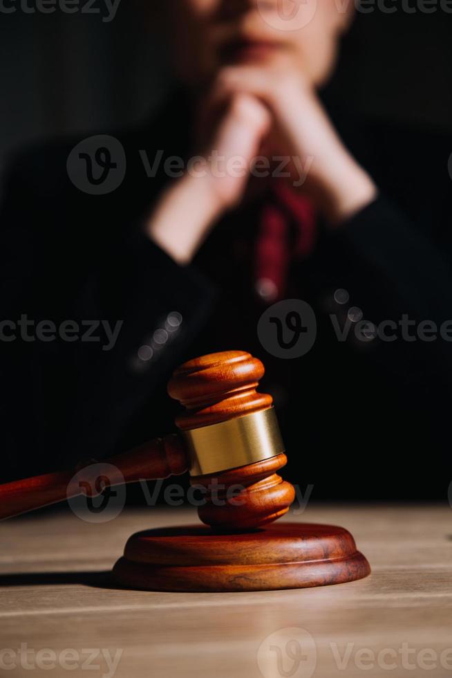 concepto de justicia y derecho. juez masculino en una sala de audiencias con el mazo, trabajando con computadora y teclado de acoplamiento, anteojos, en la mesa a la luz de la mañana foto