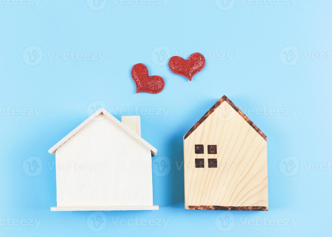 flat lay of two wooden model houses with red glitter hearts on blue background. dream house , home of love, strong relationship, neighboring houses, valentines. photo