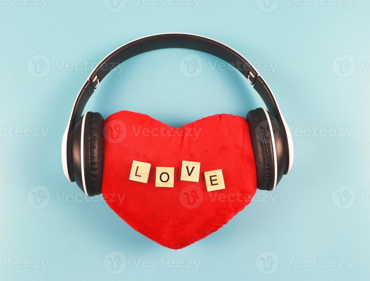 flat lay of red heart pillow with wooden letter L O V E  coverd with headphones on blue  background. Love songs , podcast or valentines concept. photo