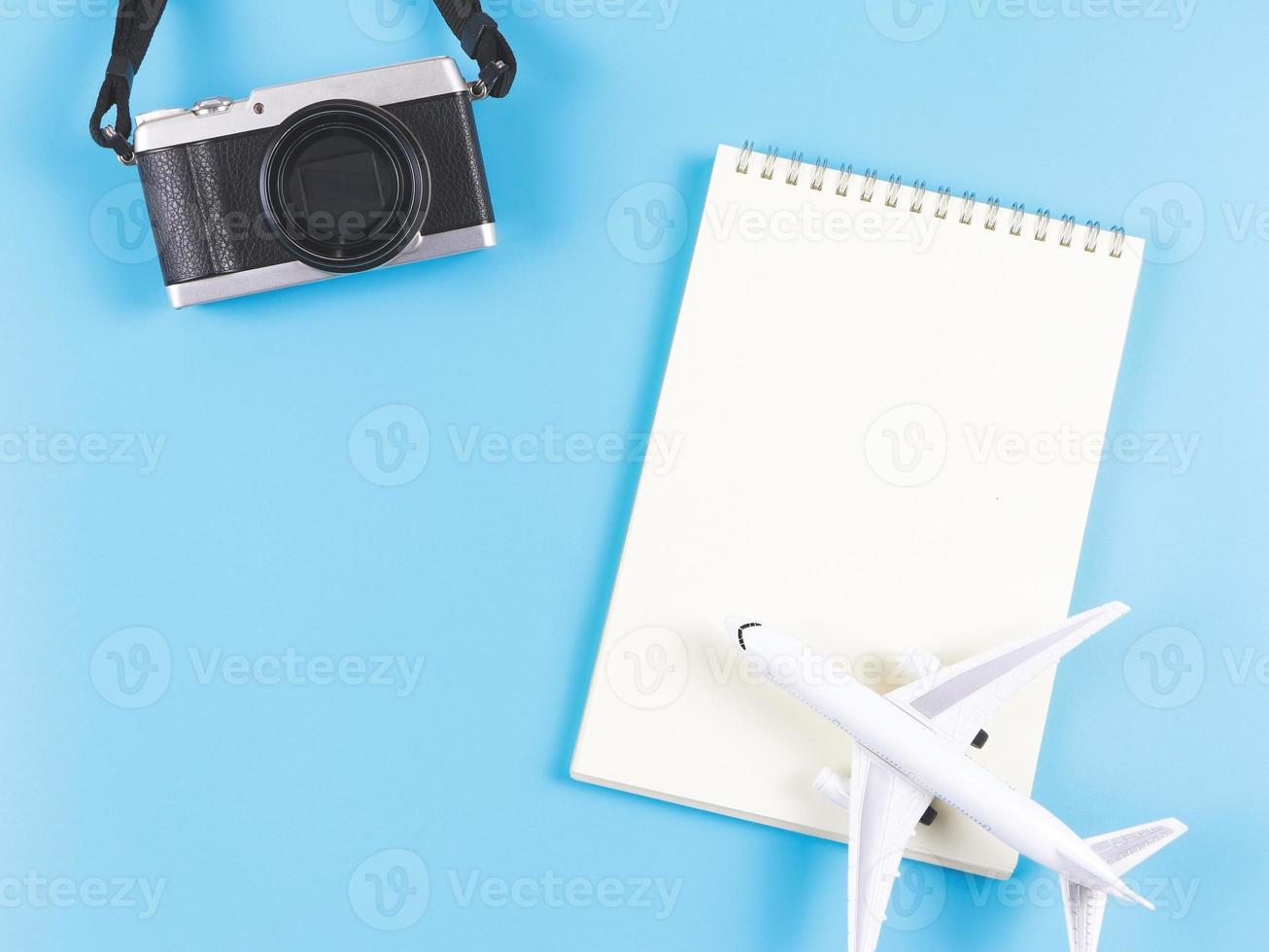 endecha plana de cuaderno abierto de página en blanco, modelo de avión y cámara sobre fondo azul. foto