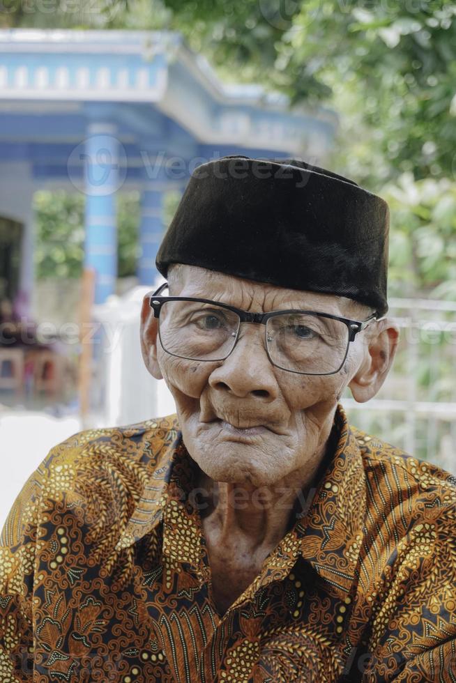 un retrato de un anciano asiático con pantalones batik y gafas foto