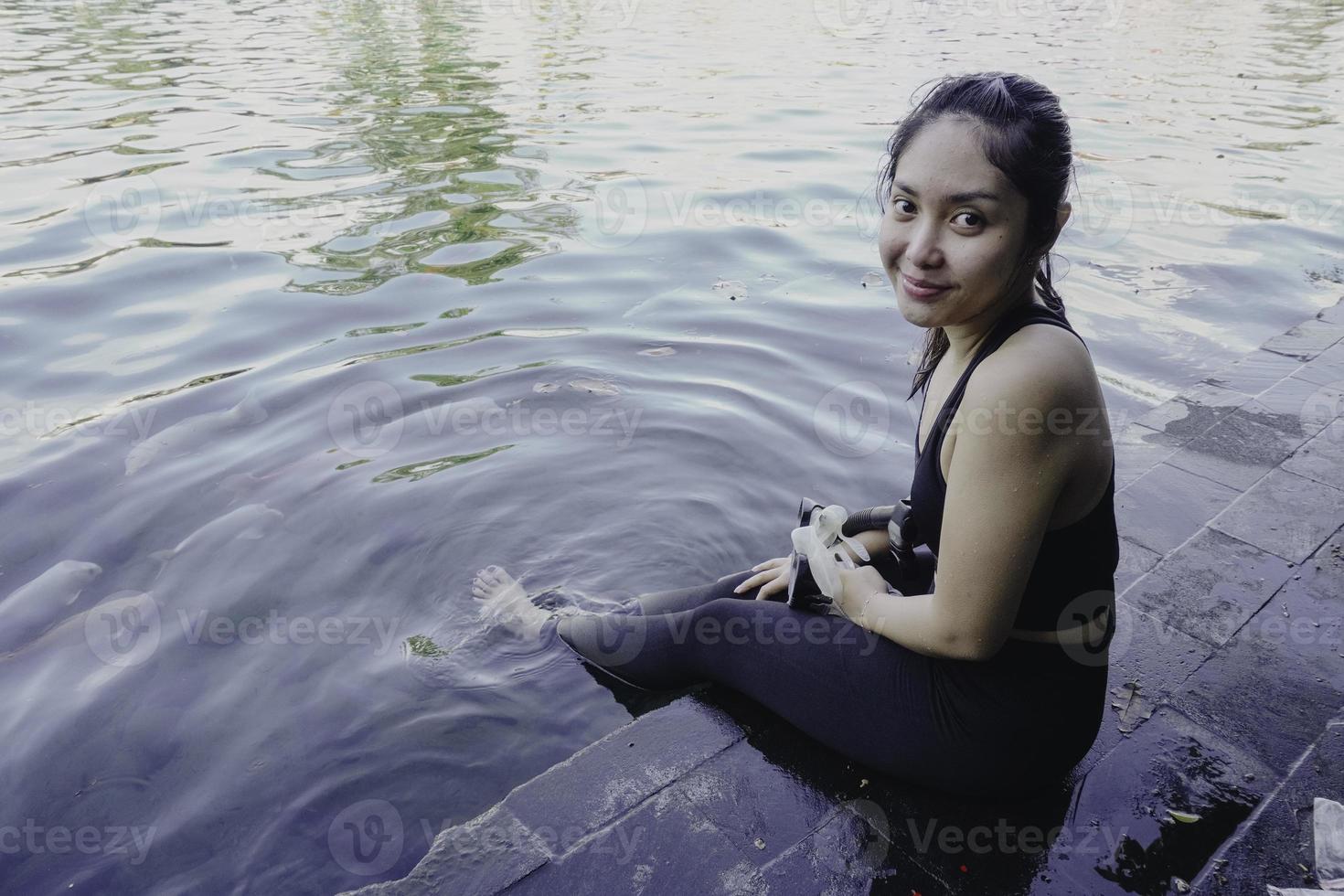 Attractive young woman sitting by the edge of a swimming pool, holding a google photo