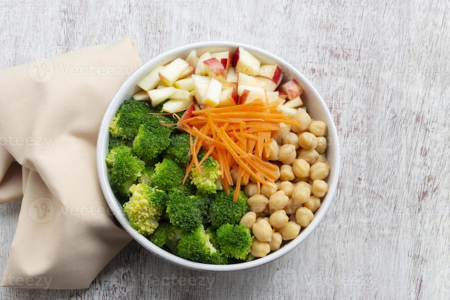 comida saludable ensalada de brócoli agregue garbanzos de manzana en un tazón blanco sobre fondo de madera. foto