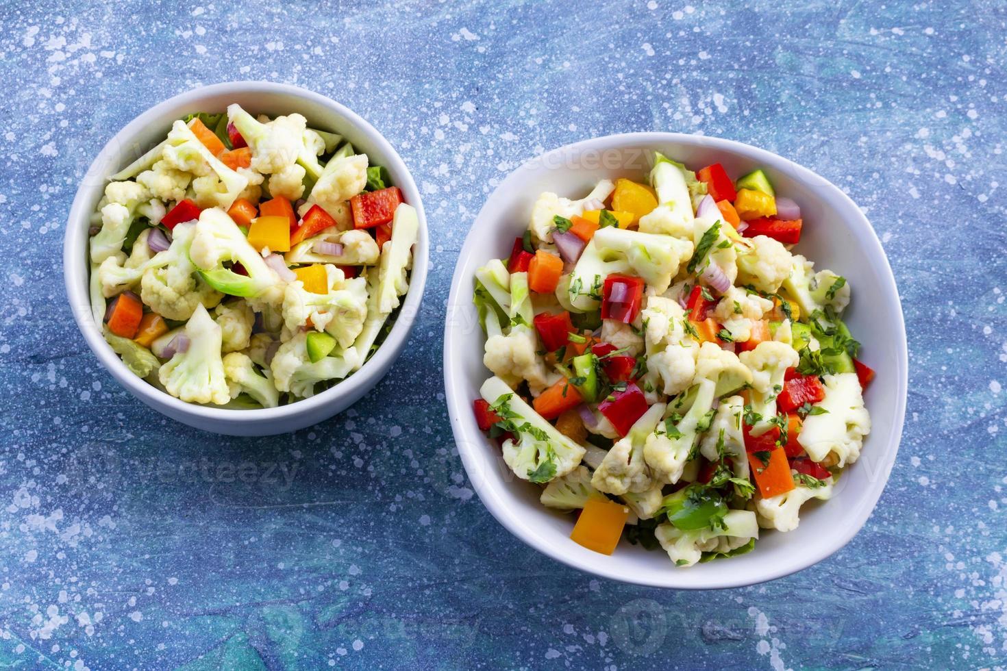 Ensalada de coliflor saludable en tazón blanco sobre fondo de madera azul. foto