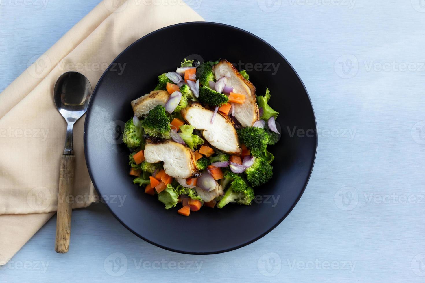 Healthy food chicken salad has vegetables in black bowl on blue wood background. photo