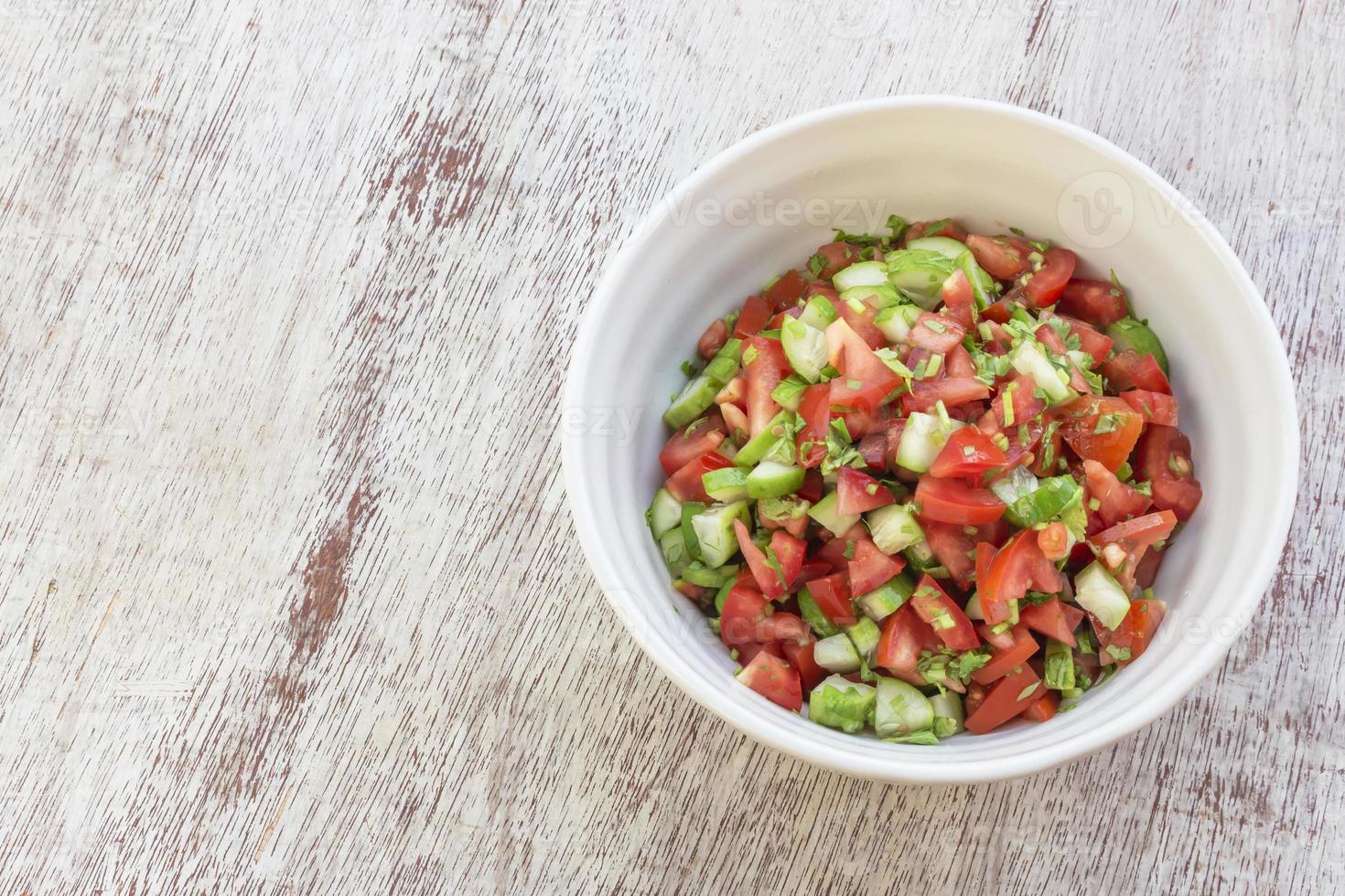 Ensalada de tomate y pepino de alimentos saludables en un tazón sobre fondo de madera blanca. foto