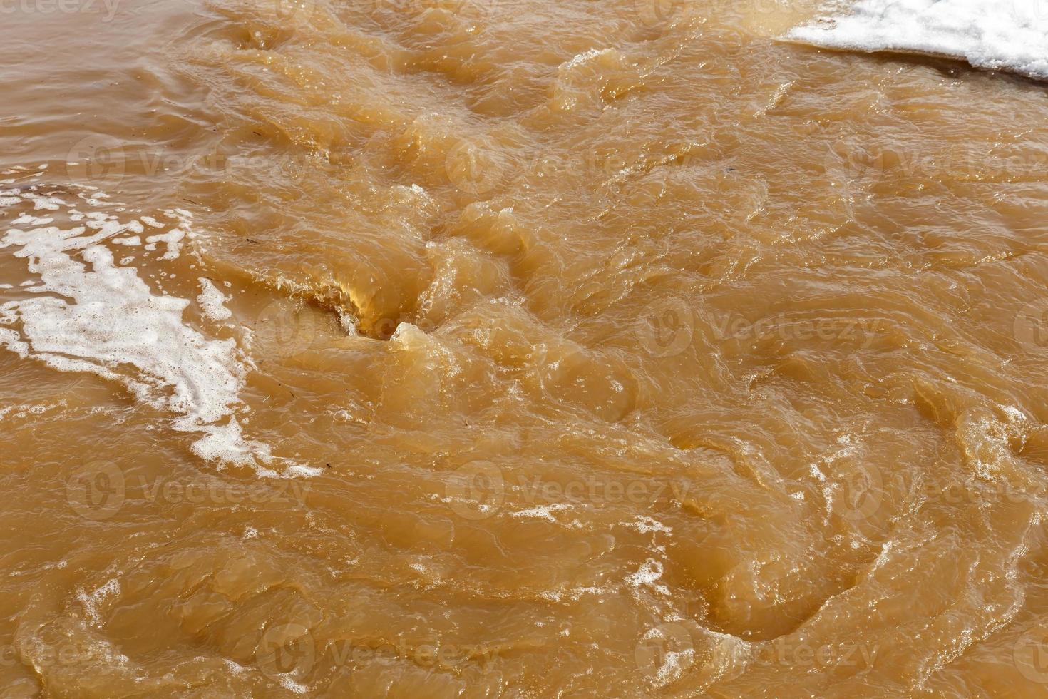 Muddy river water. Spring flood. Dirty muddy water with whirlpool and white foam close-up. photo