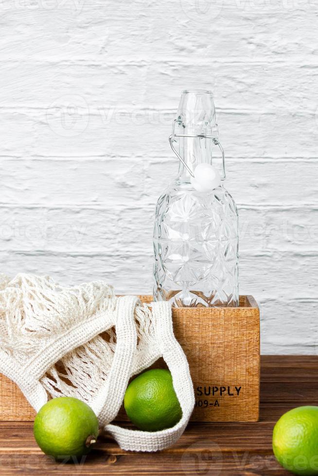 Lemonade bottle in crate with green limes on wooden table. photo