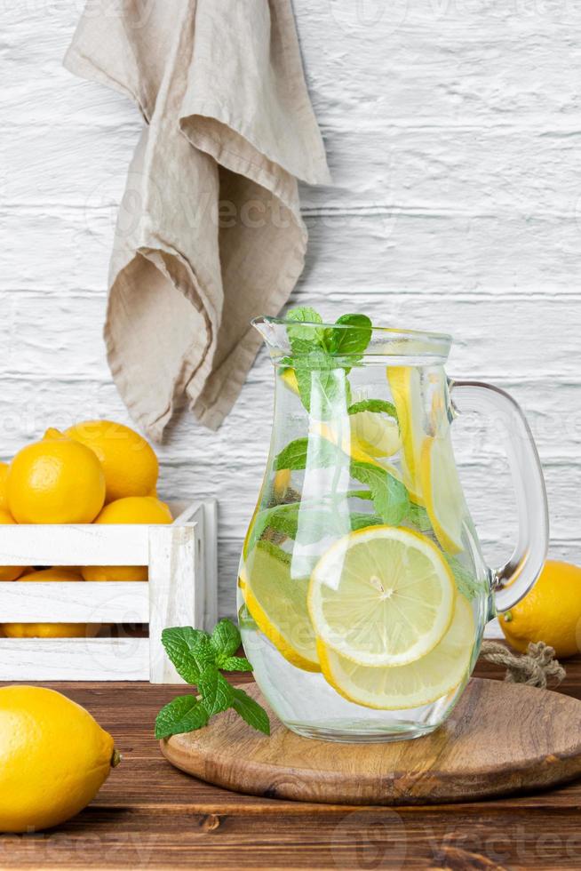 Lemonade with mint in jug and lemons in crate on wooden table. photo