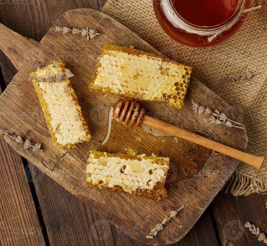 wax bee honeycomb with honey on wooden board and wooden spoon, brown table, top view photo