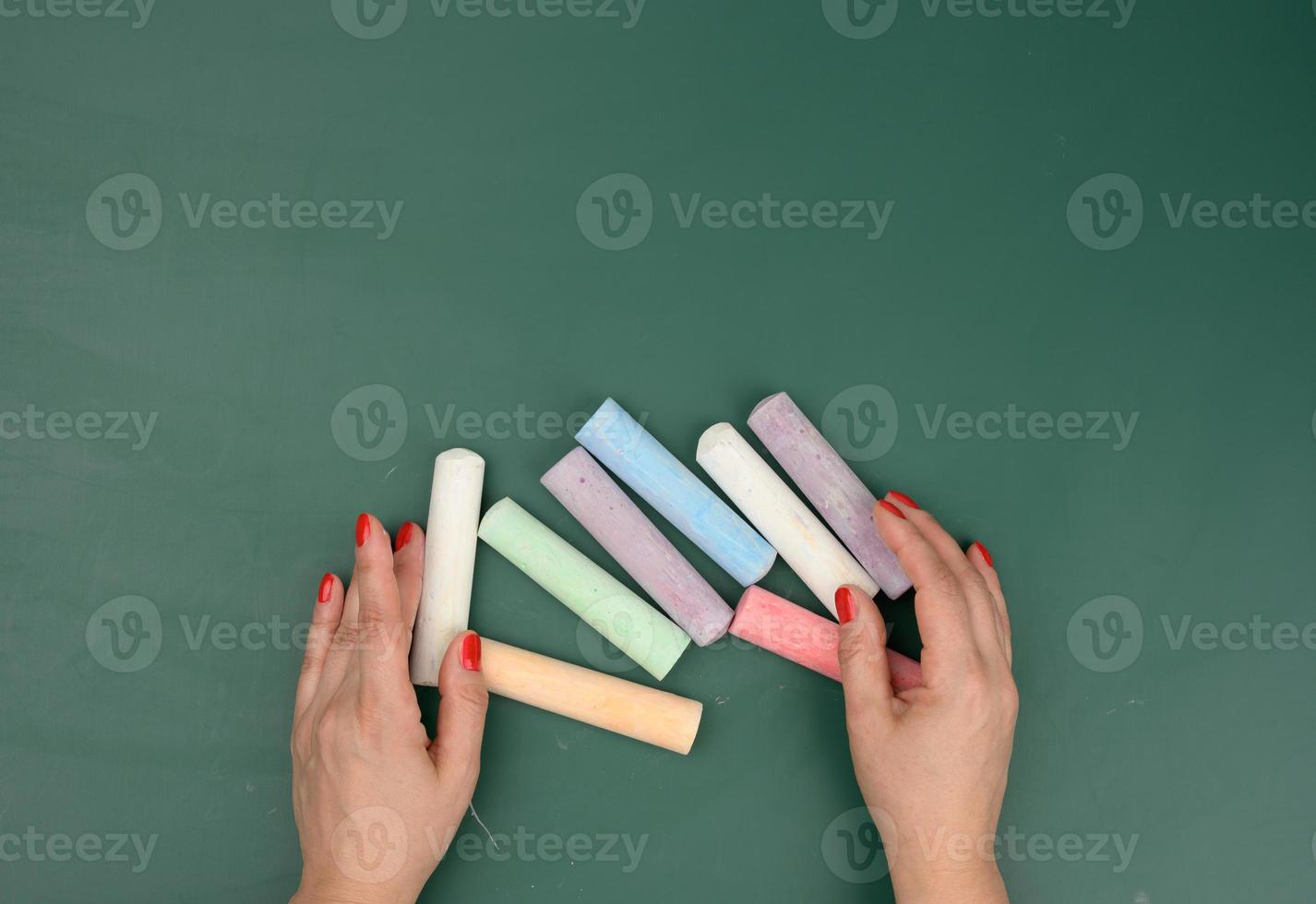 hand holds a piece of white chalk on the background of an empty green chalk board photo