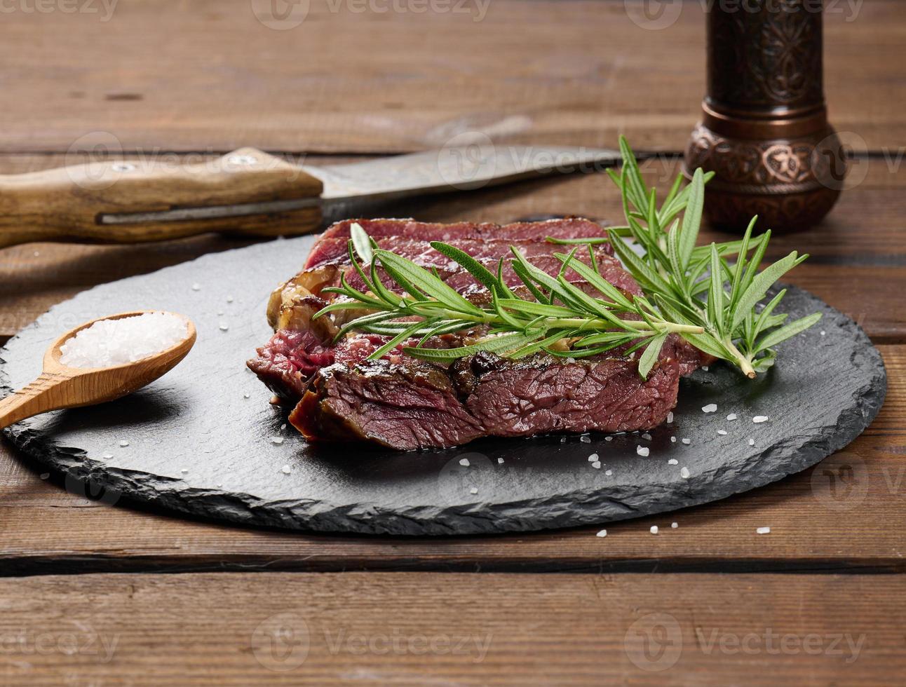 fried piece of beef ribeye cut into pieces on a black board, rare degree of doneness. Delicious steak photo