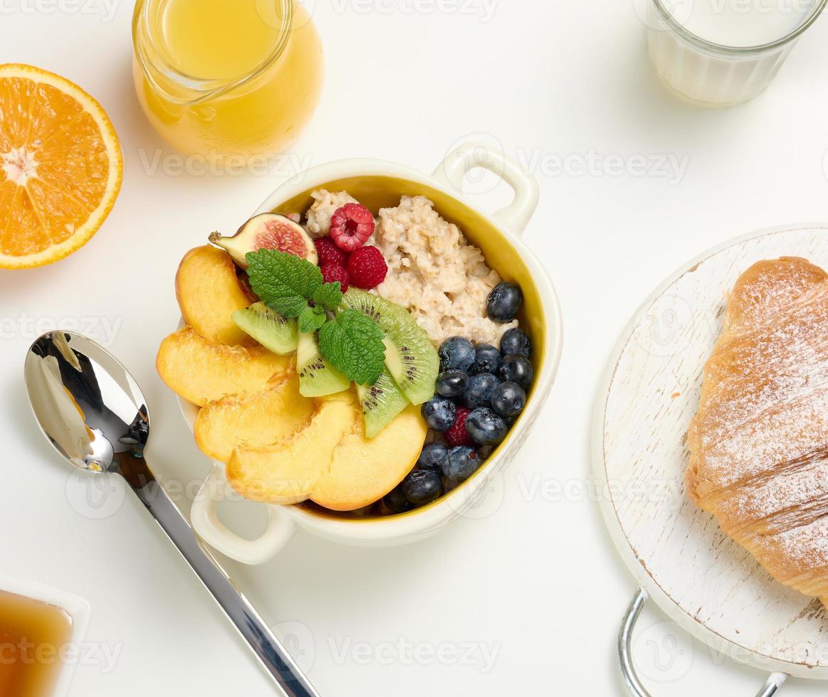 plato con avena y fruta, media naranja madura y jugo recién exprimido en un decantador de vidrio transparente, miel en un bol sobre una mesa blanca. foto