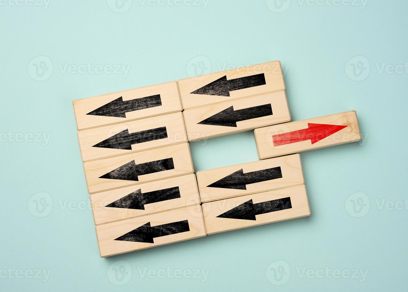 wooden cubes with black arrows in one direction and one block with a red arrow in the opposite direction. Concept of difference, uniqueness photo