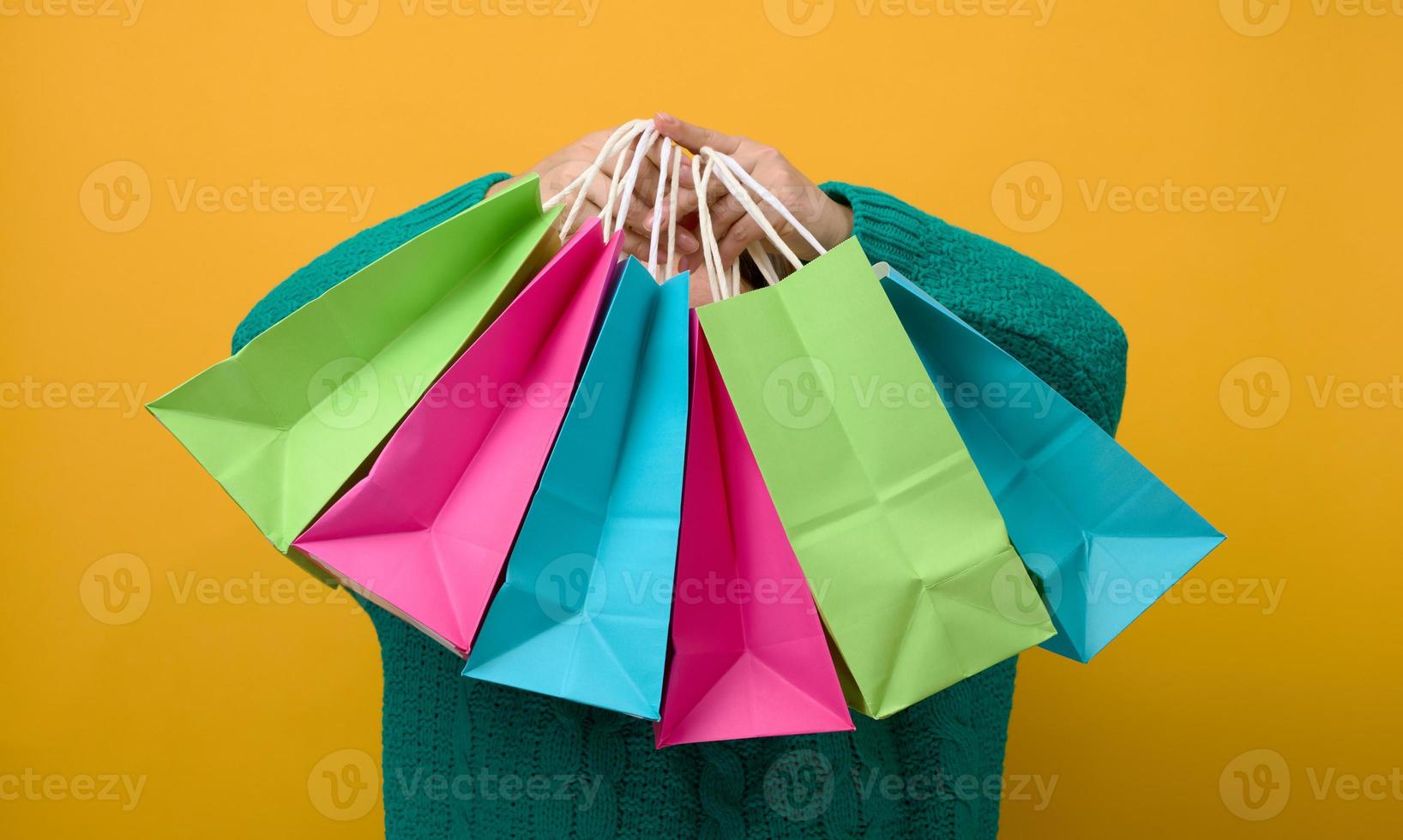 una mujer con suéter sostiene una bolsa de papel sobre un fondo amarillo y muestra un gesto similar con la mano. compras venta de temporada foto