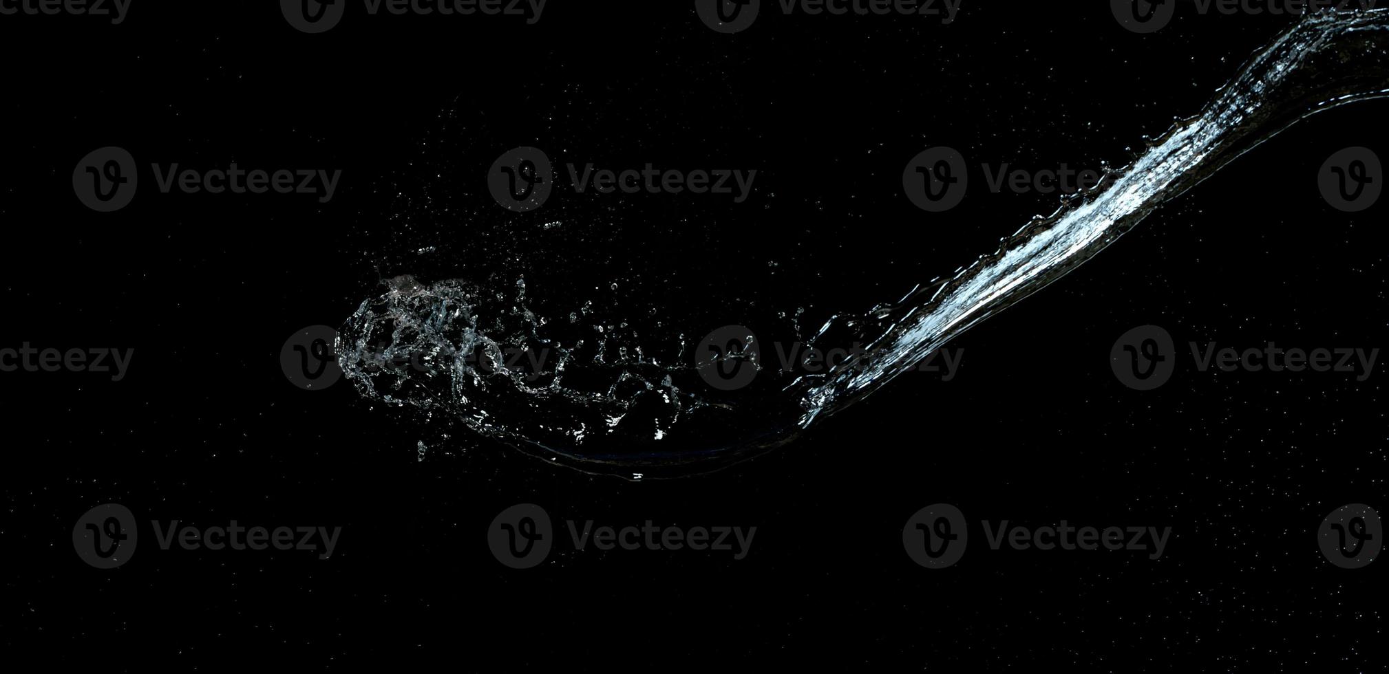 jet of transparent water with small drops and splashes on a black background photo