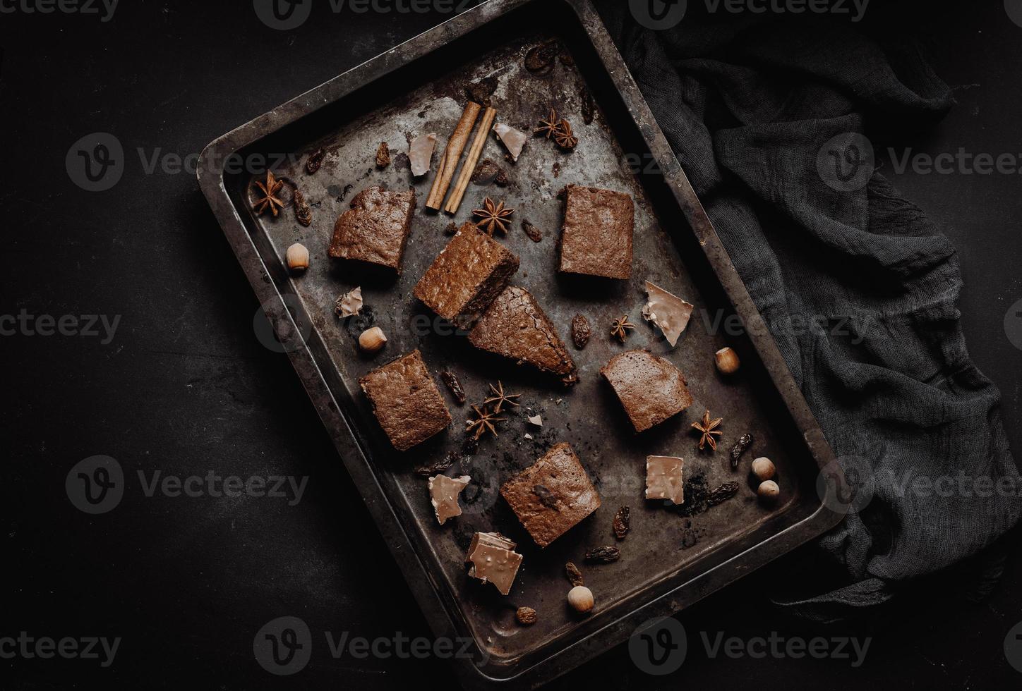 trozos de pastel de brownie de chocolate al horno en una bandeja de metal para hornear sobre una mesa negra, vista superior foto