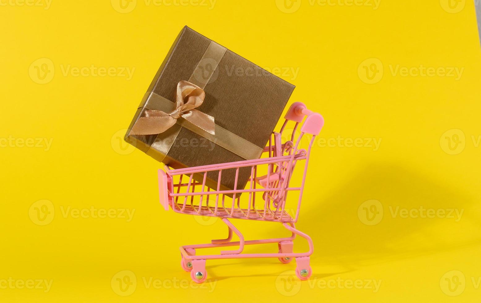 brown gift box with a silk bow in a miniature metal trolley on a yellow background photo
