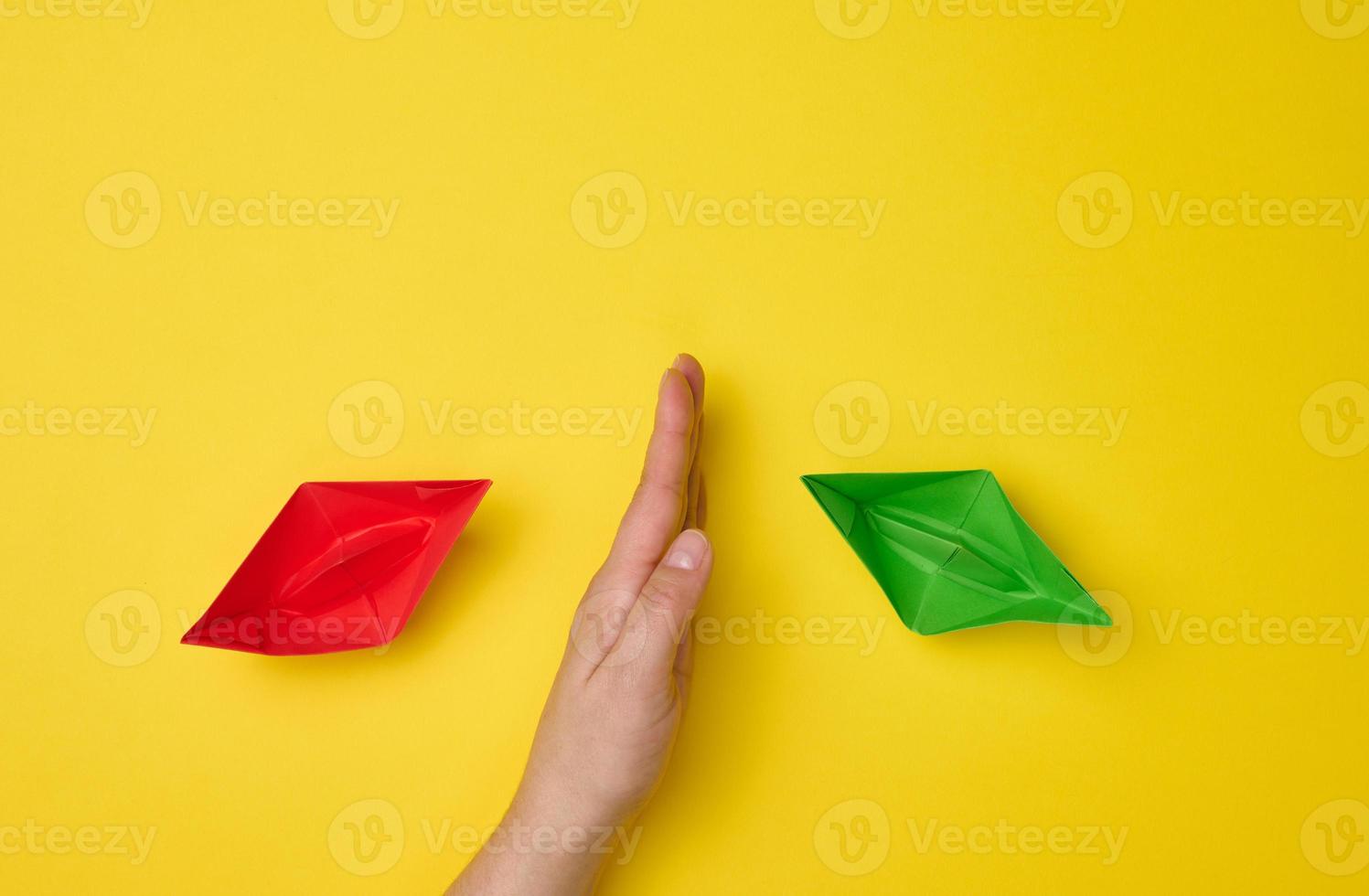 female hand between paper boats on a yellow background, the concept of reconciliation of the parties, the search for compromises. The role of the negotiator in the dialogue photo