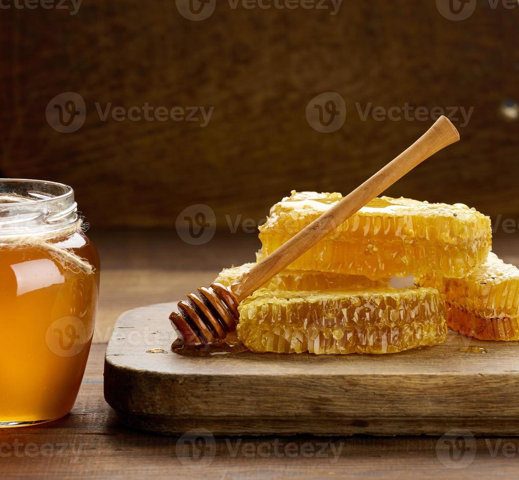 panal de cera con miel en tablero de madera y cuchara de madera, mesa marrón foto