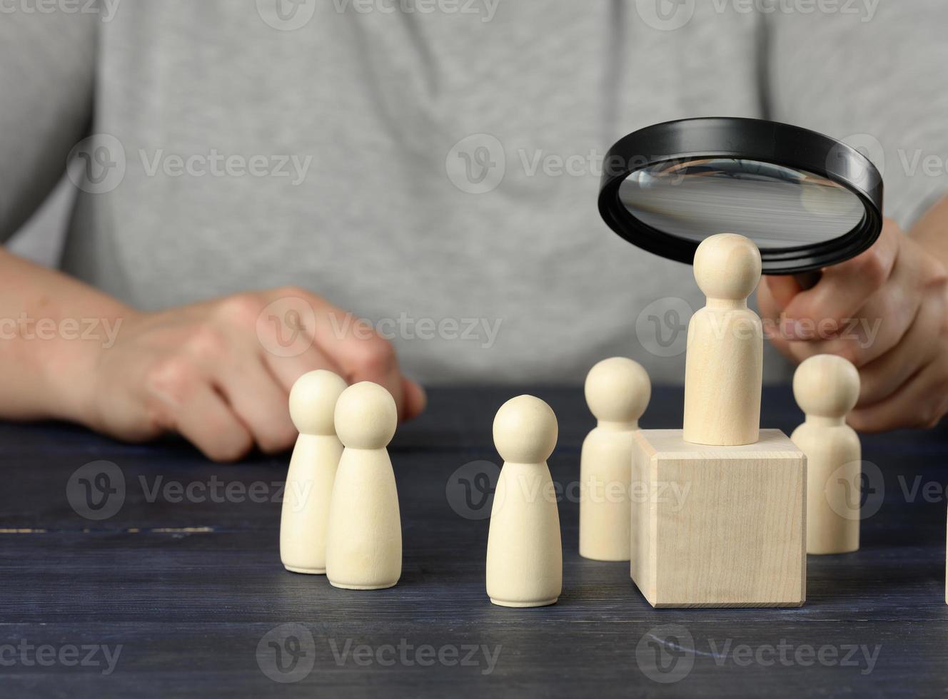 a hand with a magnifying glass examines unique and talented wooden men in the crowd photo