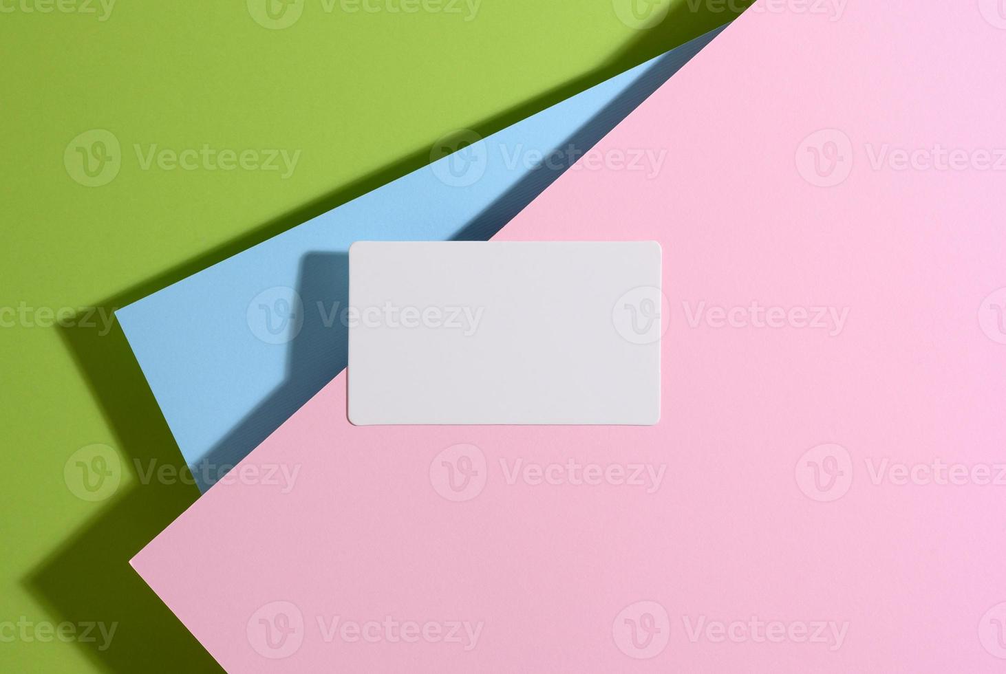 blank rectangular business card lies on a modern bright green background with blue and pink sheets of paper with a shadow photo