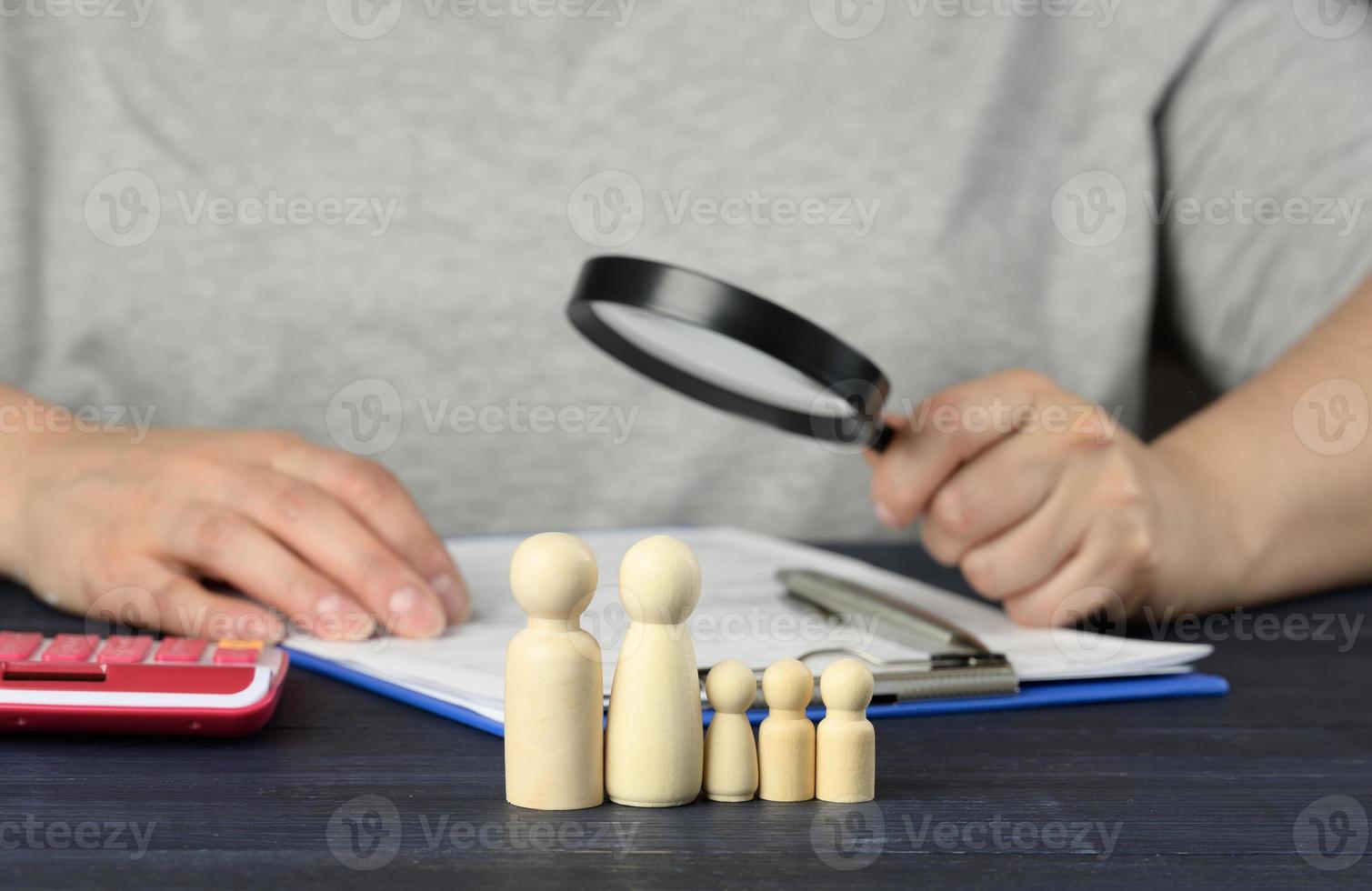 wooden figurines of little men family on the background of a man with a magnifying glass, who will examine the documents. photo