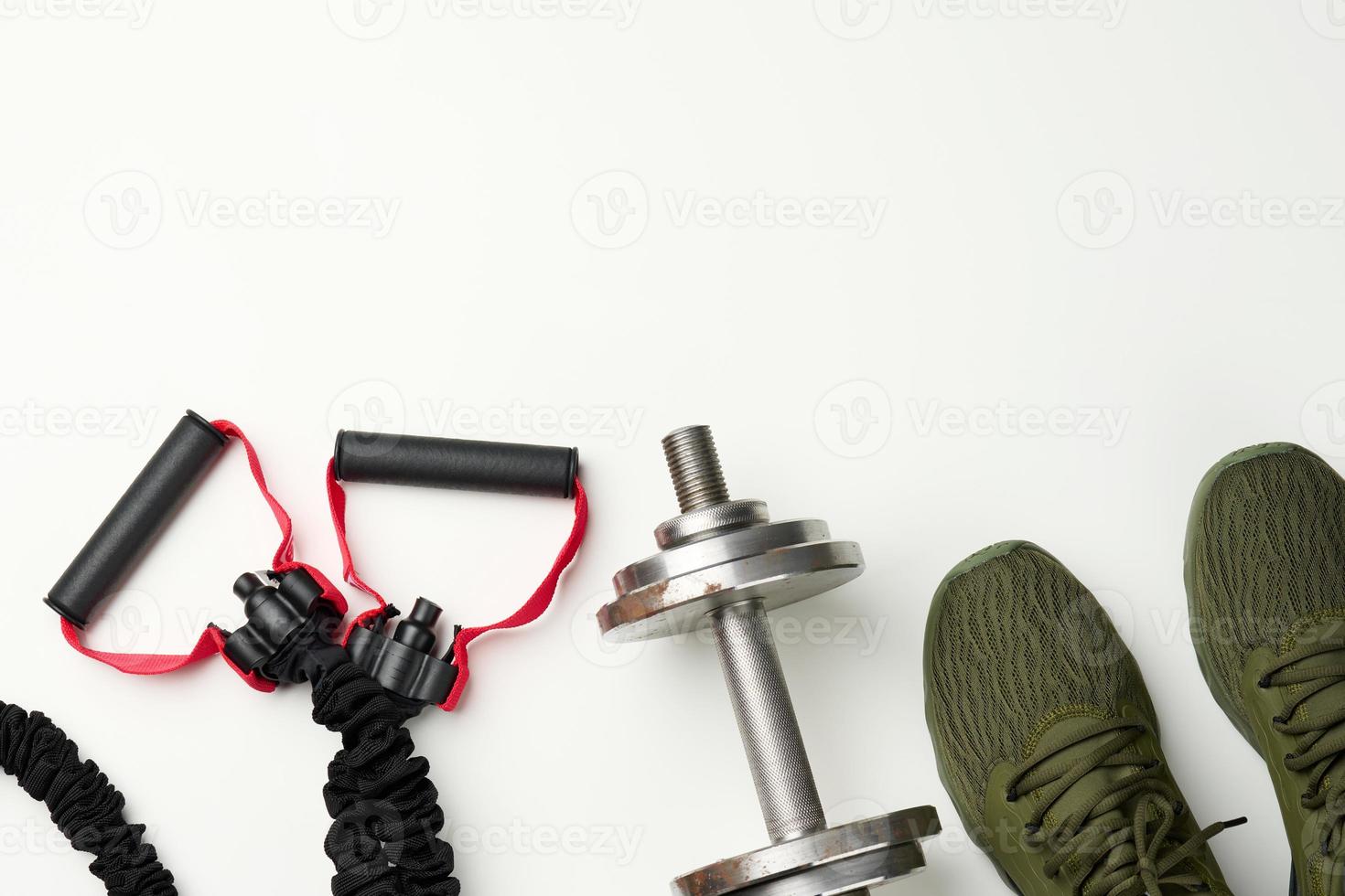 pair of green textile sneakers and a metal dumbbell on a white background, top view. Shoes for sports photo