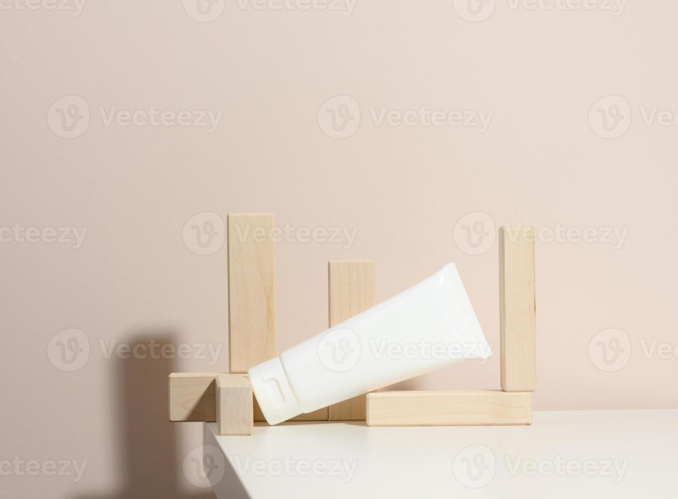 empty white plastic tubes for cosmetics on a beige background with wooden blocks. Packaging for cream, gel, serum, advertising and product promotion, mock up photo