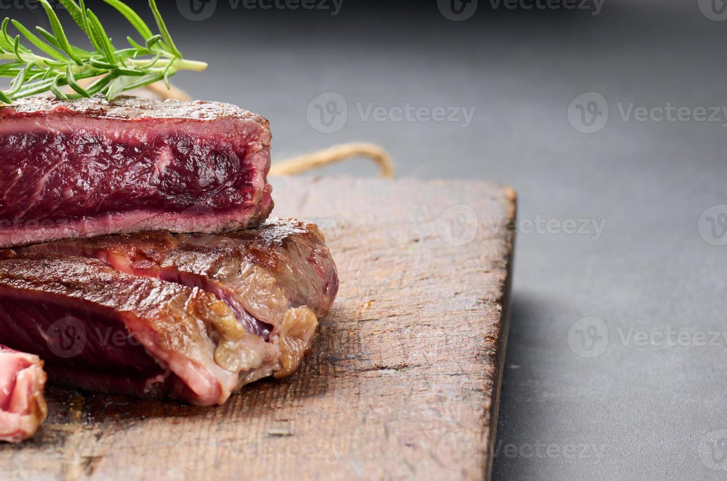 fried piece of beef ribeye, cut into pieces on a brown wooden board, rare doneness photo