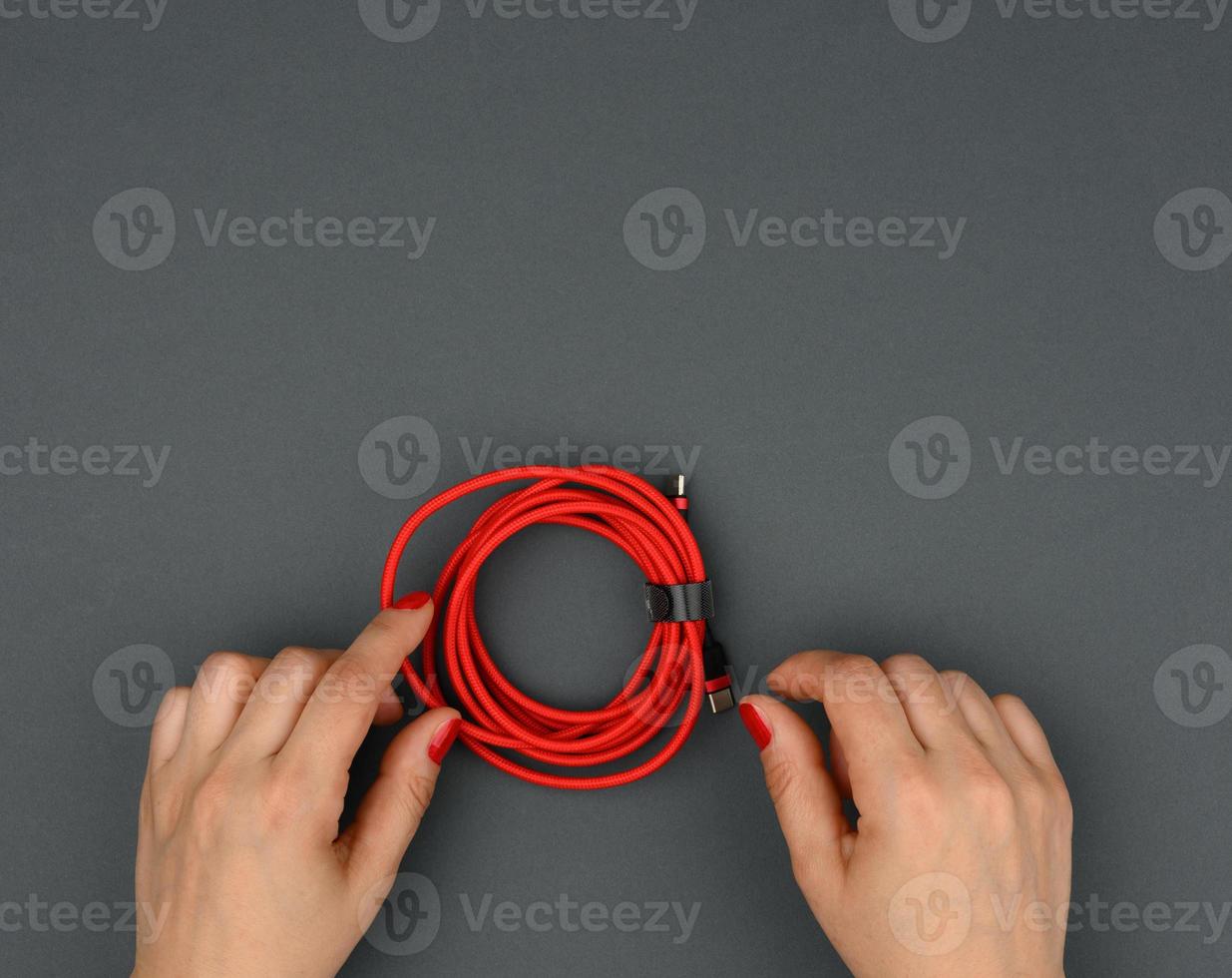 female hand holds twisted cable for charging mobile devices in a red textile wrapper on a black background photo