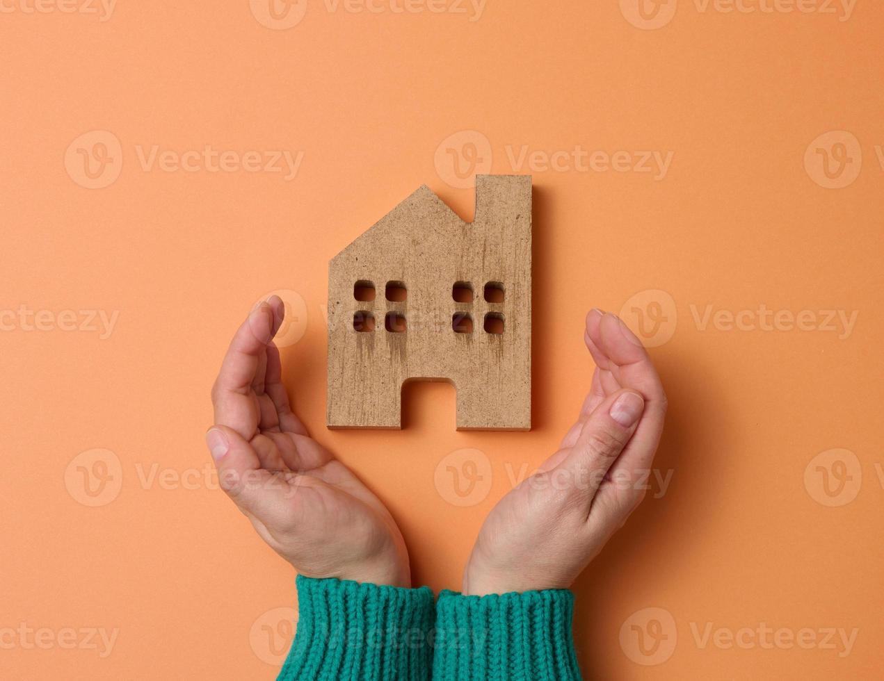 female hands folded to each other over a wooden miniature model house on a brown background. Real estate insurance concept, environmental protection, family happiness photo