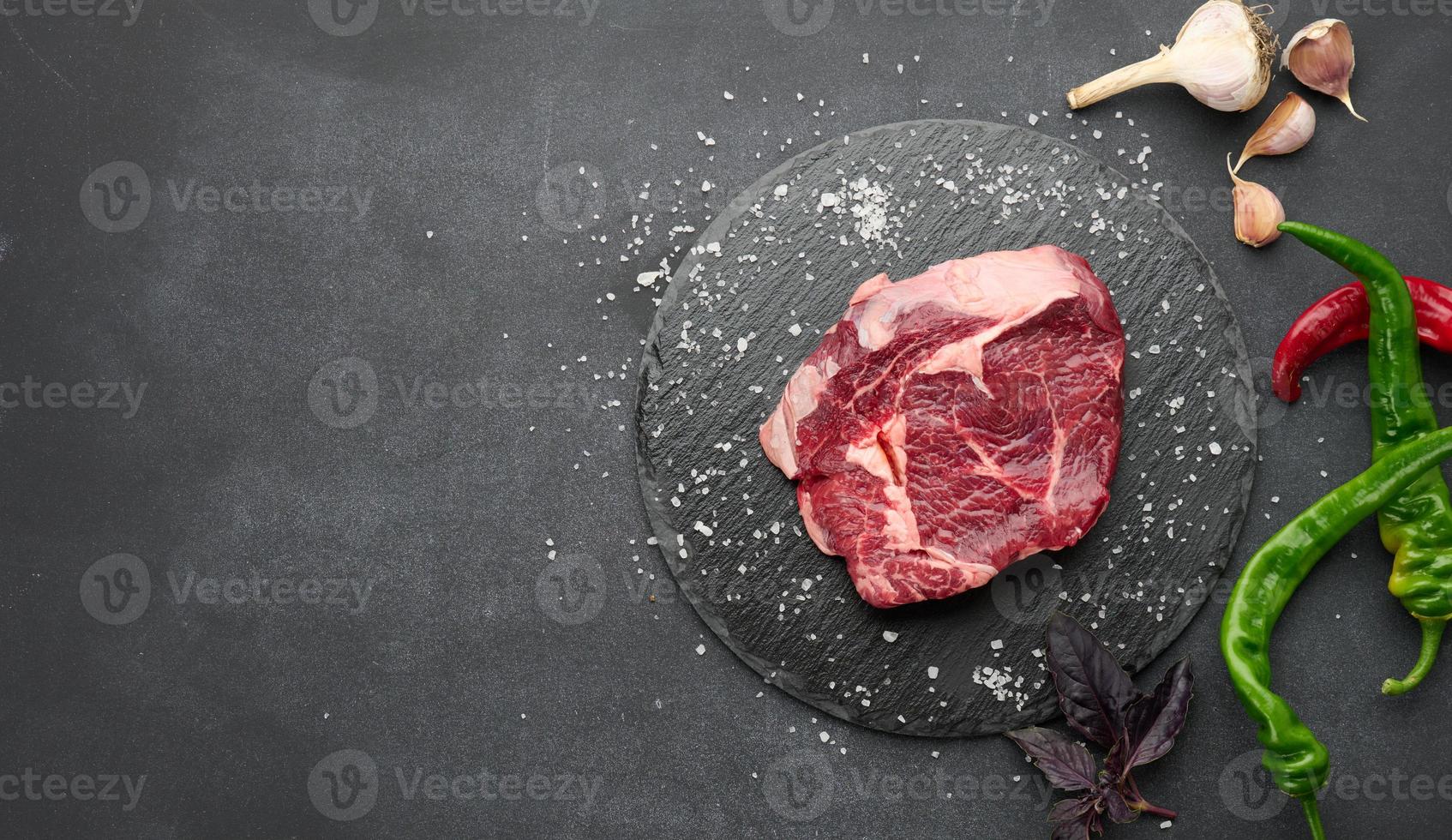 raw piece of beef ribeye with rosemary, thyme on a black table, top view photo