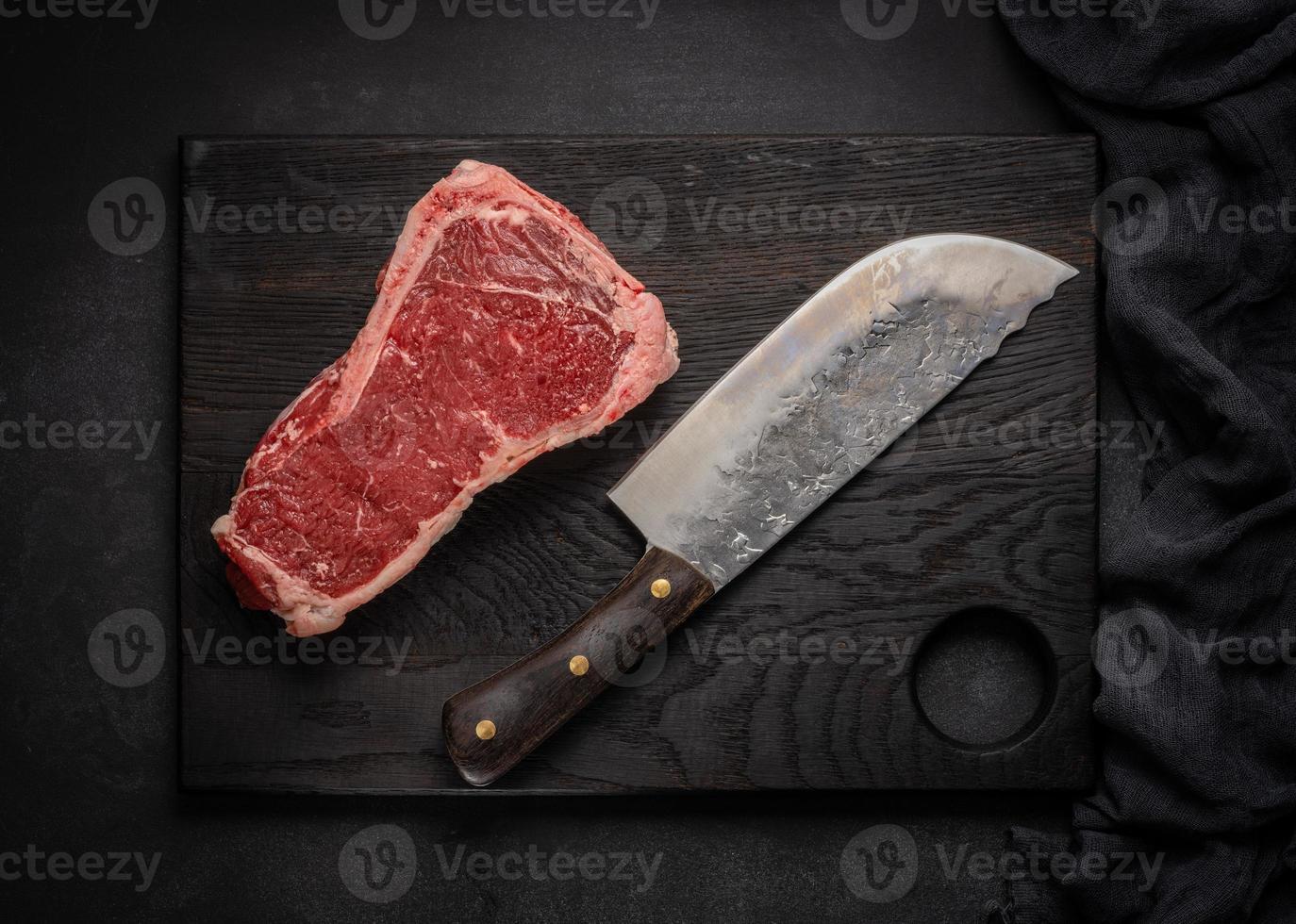 Raw juicy piece of beef meat on the bone lies on a wooden cutting board on a black background photo