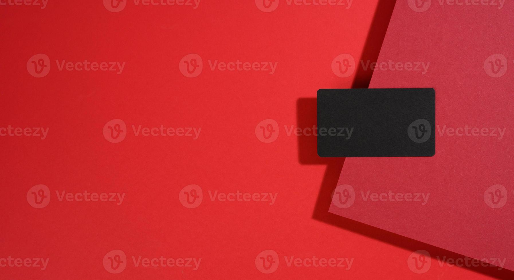 blank black rectangular business card lies on a modern red background with red sheets of paper with a shadow. Business template photo